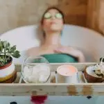 Woman relaxing in a bathtub with a candle and plants, enjoying a serene spa experience.